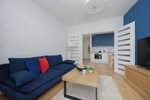 A modern living room with a blue sofa, a coffee table, and a TV on a wooden stand. - Stylish Apartment with Air Conditioning | Parking | Close to the City Centre (Warszawa)