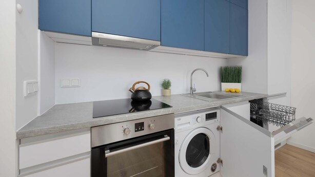 A compact kitchen with a built-in oven, a washing machine, and a sink. - Stylish Apartment with Air Conditioning | Parking | Close to the City Centre (Warszawa)