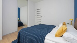 A bedroom with a bed, a wardrobe, a mirror, and a bedside table with a lamp. - Stylish Apartment with Air Conditioning | Parking | Close to the City Centre (Warszawa)