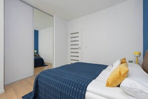 A bedroom with a bed, a wardrobe, a mirror, and a bedside table with a lamp. - Stylish Apartment with Air Conditioning | Parking | Close to the City Centre (Warszawa)