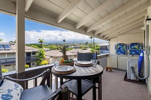 A balcony with a table set for two, overlooking a residential area with houses and greenery. - Kona Shores#223: Top Floor, Split AC, Remodeled, Washer/Dryer (Kailua Kona)
