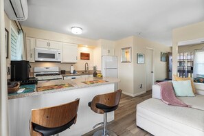 Eine kompakte Küche mit einer zentralen Kochinsel, zwei Barhockern, einem weißen Sofa und einem Balkon mit Blick.