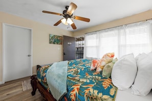 A bedroom with a bed, a ceiling fan, a door, and a window with curtains. - Kona Shores#223: Top Floor, Split AC, Remodeled, Washer/Dryer (Kailua Kona)