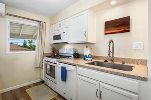 A compact kitchen with white cabinets, a stainless steel sink, a stove, and a microwave. - Kona Shores#223: Top Floor, Split AC, Remodeled, Washer/Dryer (Kailua Kona)