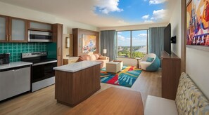 A modern kitchen with a central island, a dining area with a colorful rug, and a living space with a sofa and a view of the city. - Orlando | Park View Magic Stay | Pool + Monorail (Lake Buena Vista)