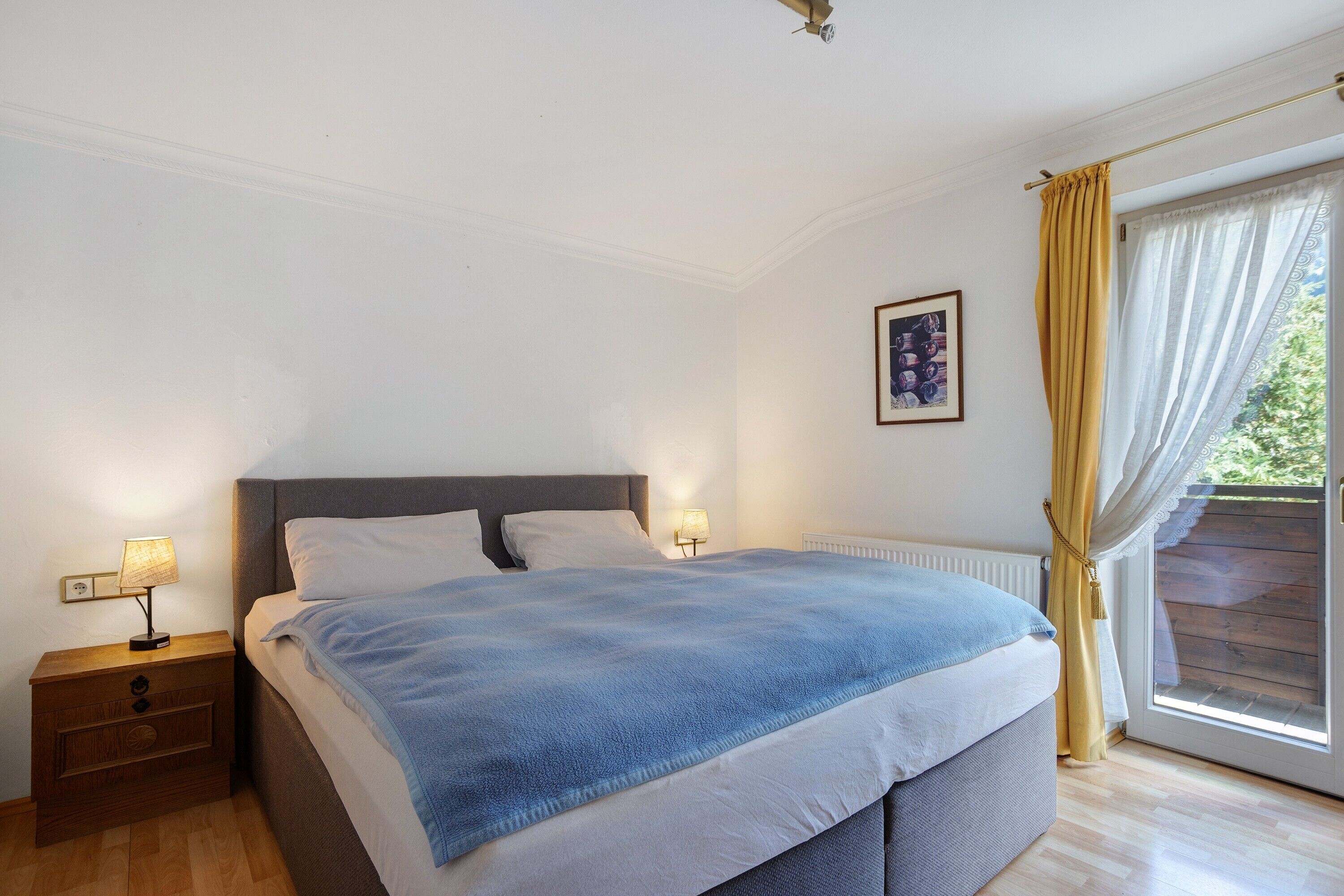 A bedroom with a bed, bedside lamps, a radiator, and a window with curtains.