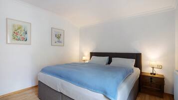 A neatly made bed with a blue blanket, two bedside lamps, and two framed floral paintings on the wall.