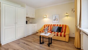 Un espacio habitable compacto con kitchenette, un sofá a rayas, una pequeña mesa con un objeto decorativo y dos lámparas fijadas a la pared.