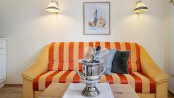 Una habitación con un sofá a rayas, dos lámparas fijadas a la pared, un cuadro enmarcado y una mesa con una jofaina de plata.