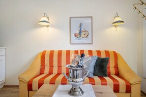 Una habitación con un sofá a rayas, dos lámparas fijadas a la pared, un cuadro enmarcado y una mesa con una jofaina de plata.
