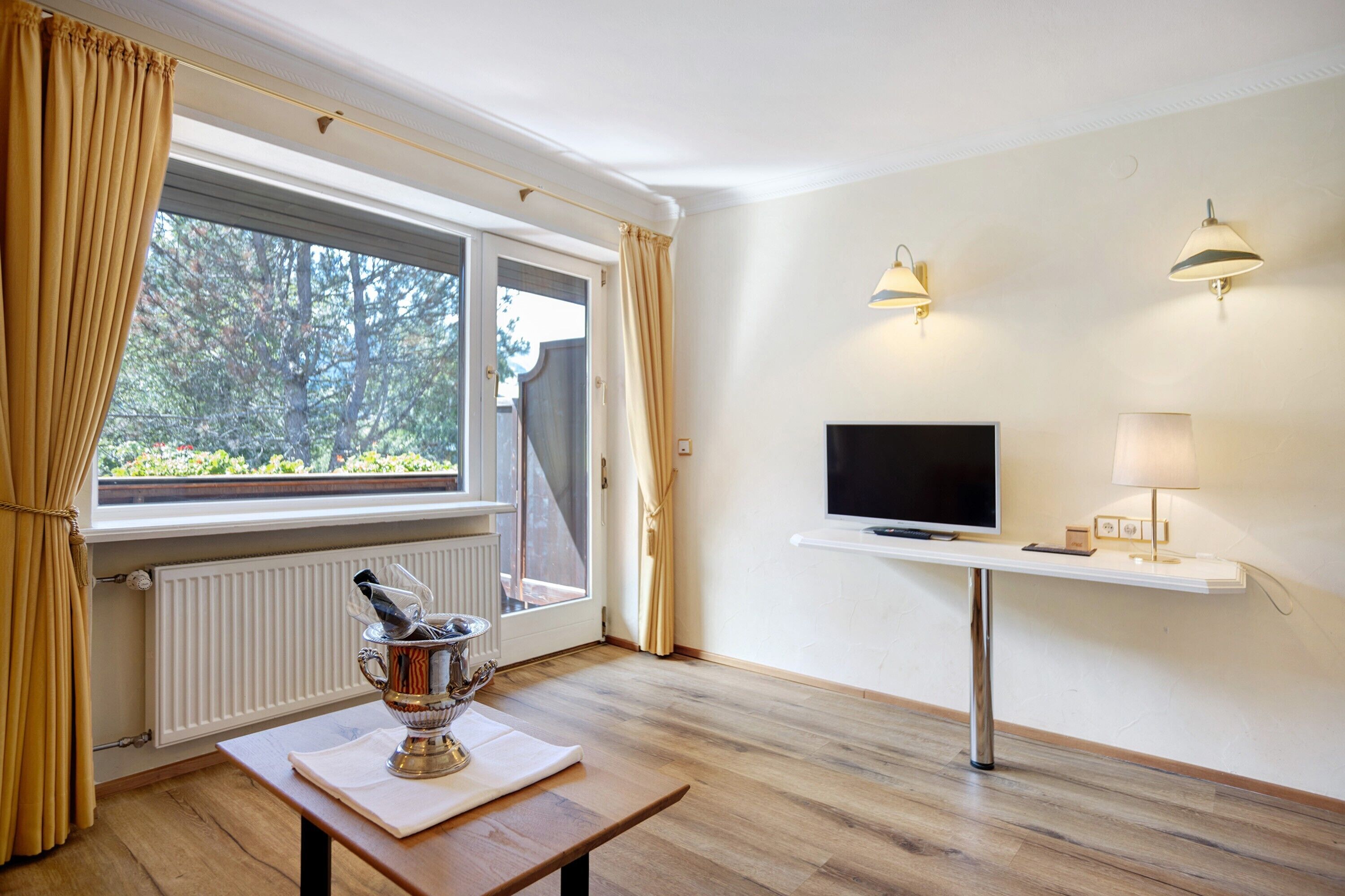 Ein Zimmer mit Holzboden, einem Tisch mit einer Glas-Trophäe, einem Fernseher auf einem Schrank und Vorhängen an einem Fenster.