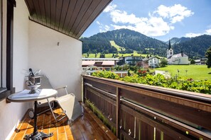 Ein Balkon mit Blick auf eine Berglandschaft, darunter eine Kirche und Wohnhäuser.