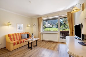 Ein Zimmer mit einer Couch, einem Tisch, einem Fernseher und einem Fenster mit Vorhängen.