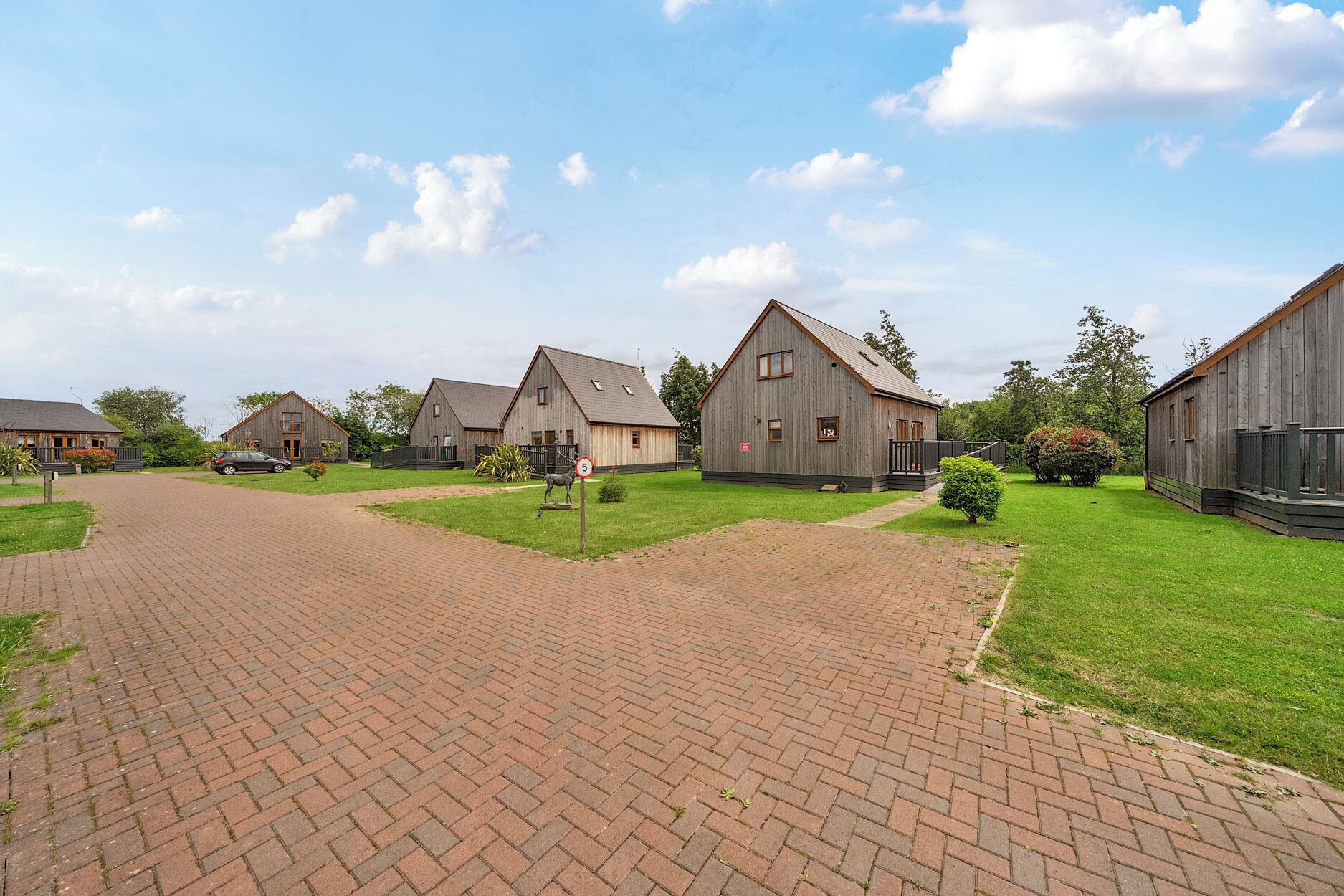 A rural setting with wooden farm buildings, paved pathways, and green lawns.