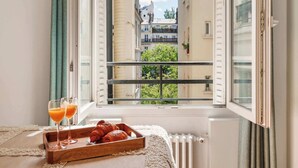 Ett fönster med utsikt över en stadsbild, ett bricka med croissanter och två glas apelsinjuice på en fönsterbräda.
