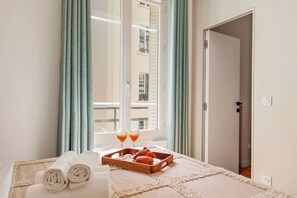 A hotel room with a bed, a tray with towels and glasses, and a view of a building through the window. - Charming 2BR - Grands Boulevards & Bonne Nouvelle (Paris)