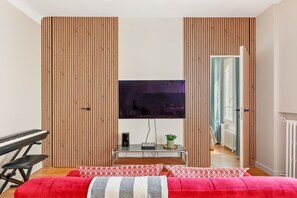 Ein modernes Schlafzimmer mit einem großen Bett, einem Fernseher, einem Schreibtisch mit Tastatur und einer Topfpflanze.
