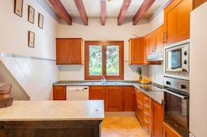 A kitchen with wooden cabinets, a built-in oven, and a window. - Rural house 'Ses Rotetes' with private pool, terrace, and private garden (Manacor)