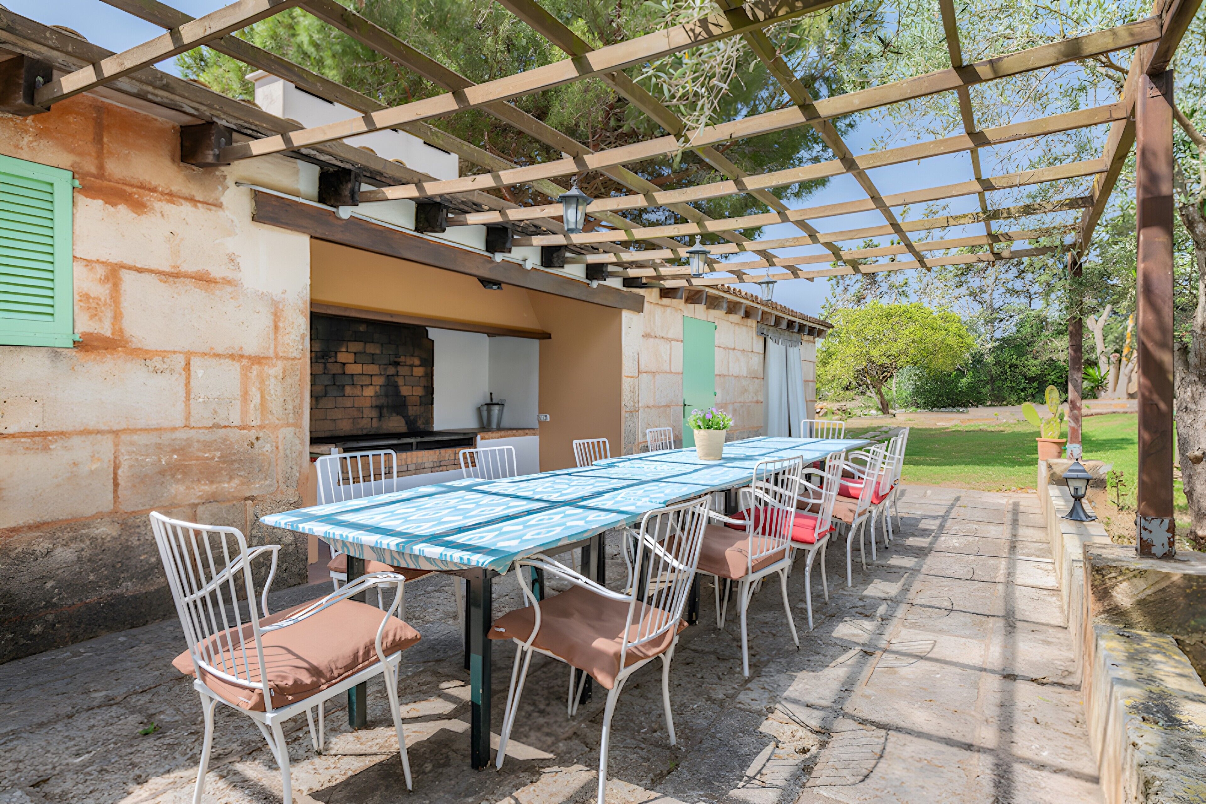 An outdoor patio with a pergola, a brick barbecue area, and a table set for dining.