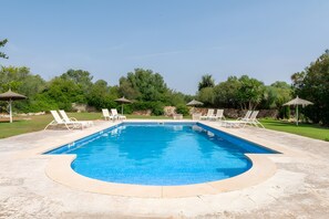 A rectangular swimming pool with a curved edge, surrounded by a stone deck. There are lounge chairs and umbrellas around the pool. - Rural house 'Ses Rotetes' with private pool, terrace, and private garden (Manacor)