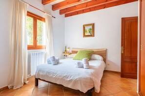 A hotel room with a bed, a window with curtains, a radiator, a bedside table with a lamp, and a door. - Rural house 'Ses Rotetes' with private pool, terrace, and private garden (Manacor)
