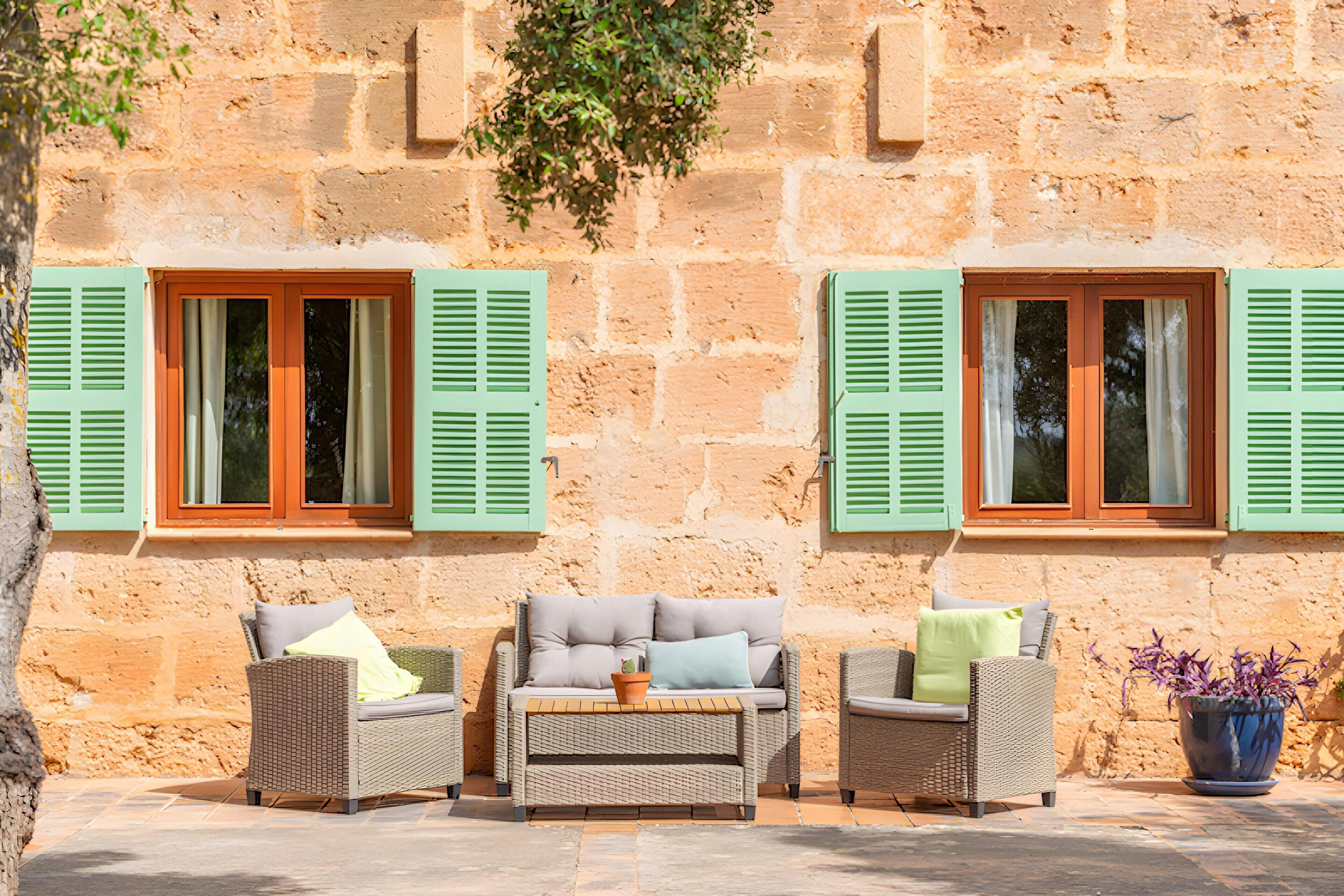A stone building with two windows and a seating area with wicker furniture.
