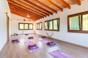 Una habitación amplia con vigas de madera en el techo, ventanas grandes y varias esterillas de yoga dispuestas en el suelo.