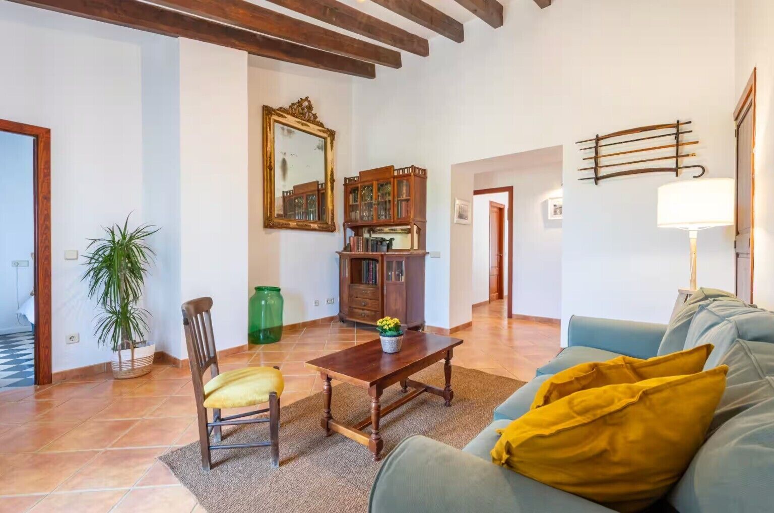 Un salon comprenant un canapé, une table basse en bois, un fauteuil, une plante en pot, un meuble avec des portes en verre et un miroir au mur.