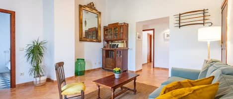 A living room with a sofa, a wooden coffee table, a chair, a potted plant, a cabinet with glass doors, and a mirror on the wall.