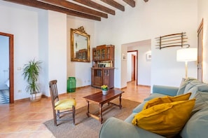 A living room with a sofa, a wooden coffee table, a chair, a potted plant, a cabinet with glass doors, and a mirror on the wall. - Rural house 'Ses Rotetes' with private pool, terrace, and private garden (Manacor)