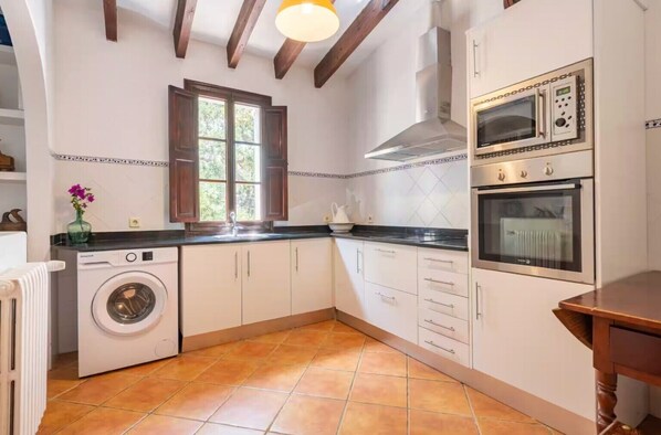 Una cocina con lavadora, horno doble y ventana con persianas de madera.
