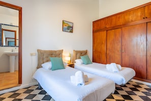 A hotel room with two beds, a wooden wardrobe, a bathroom with a sink, and a mirror. - Rural house 'Ses Rotetes' with private pool, terrace, and private garden (Manacor)