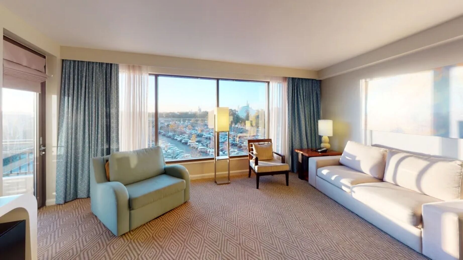A hotel room with a large window, a sofa, a chair, and a lamp.
