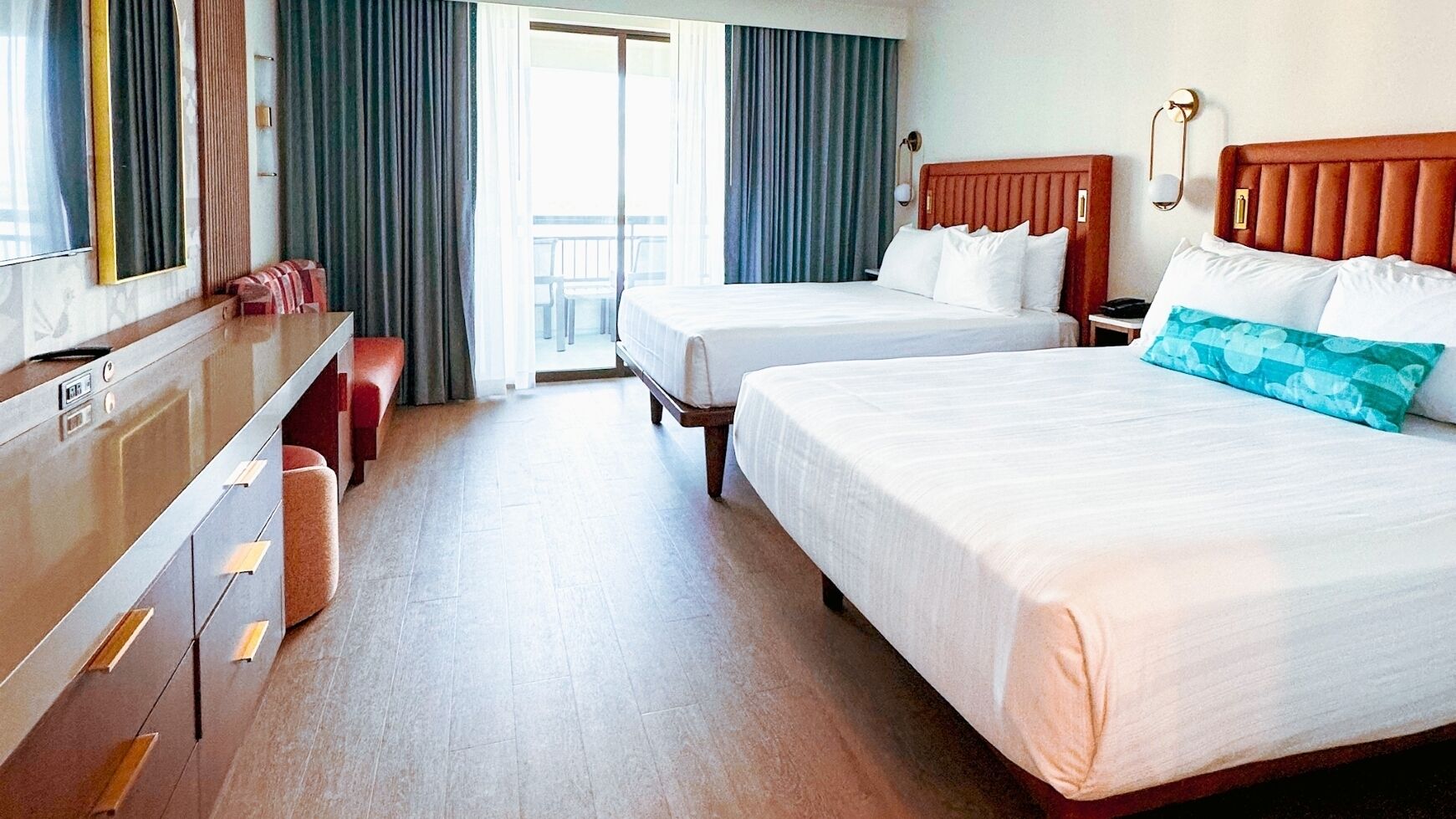 A hotel room with two beds, a desk with drawers, a chair, and a view of the outside.