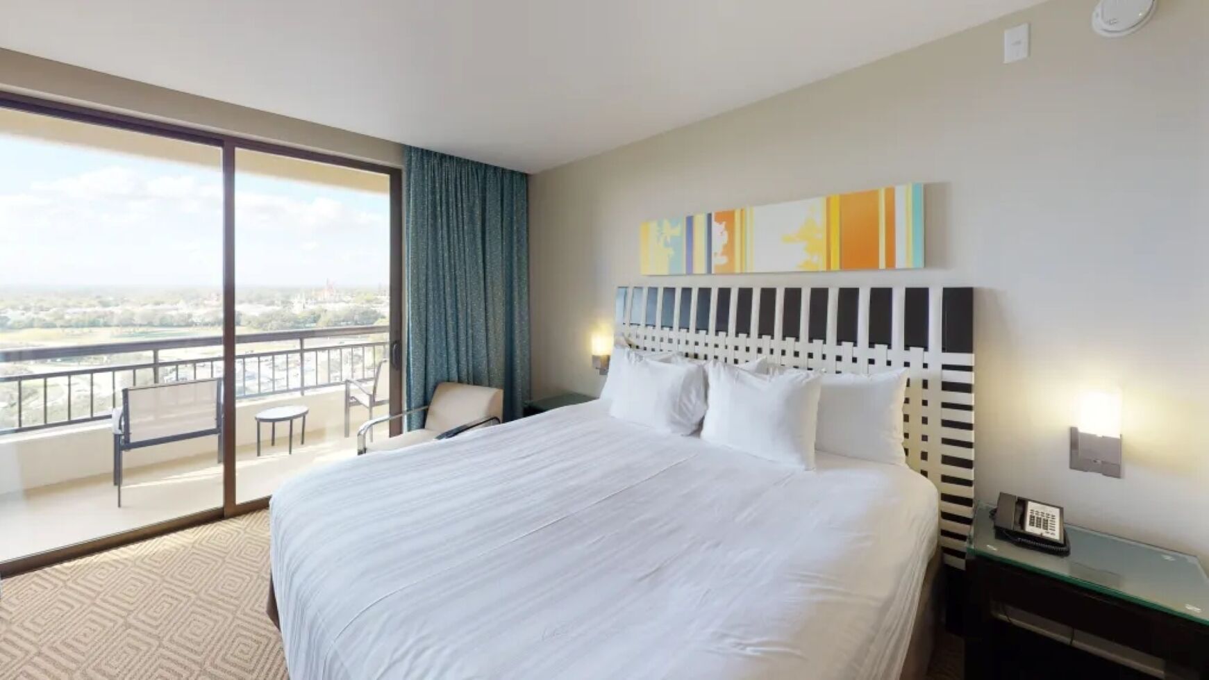 A hotel room with a large bed, a balcony with a view, a desk, and a chair.