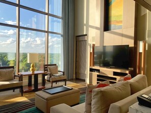 Habitación de hotel moderna con un televisor grande, asientos cómodos y vistas al exterior.