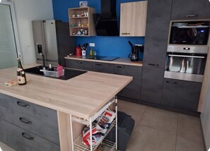 A modern kitchen with a central island, built-in appliances, and a blue accent wall. - Family home near the beaches. Pets welcome! (Assérac)