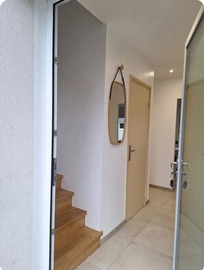 A hallway with a wooden staircase, a door, and a mirror on the wall. - Family home near the beaches. Pets welcome! (Assérac)