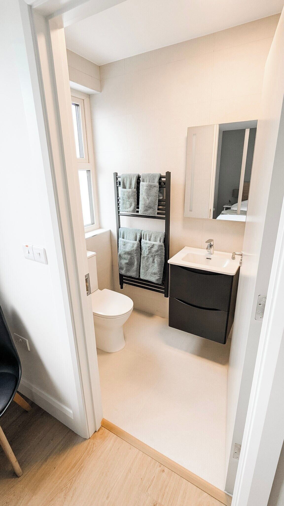 A compact bathroom with a toilet, a towel rack with towels, a sink, and a mirror.