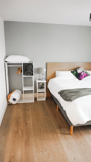 A bedroom with a bed, a nightstand, a wardrobe, and a small table with a lamp.