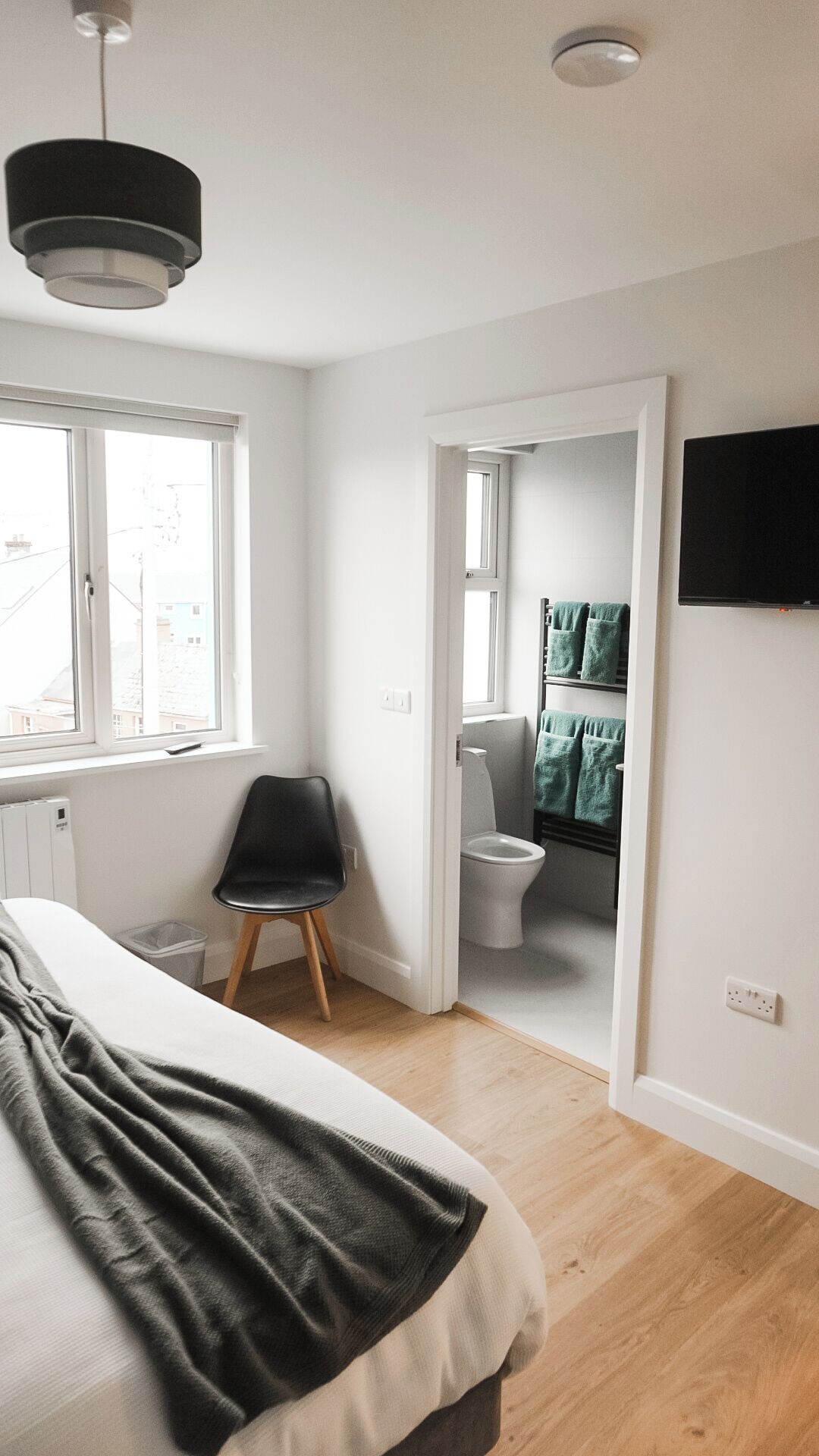 Une chambre à coucher avec un lit, une chaise, un téléviseur et une salle de bain visible à travers une porte ouverte.