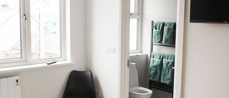 A bedroom with a bed, a chair, a television, and a bathroom visible through an open door.