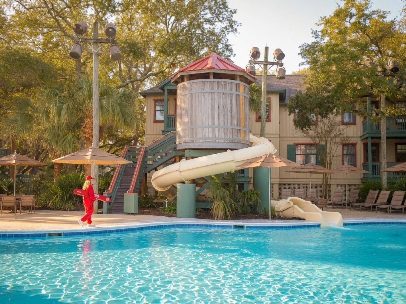 A pool area with a water slide, lounge chairs, and umbrellas.