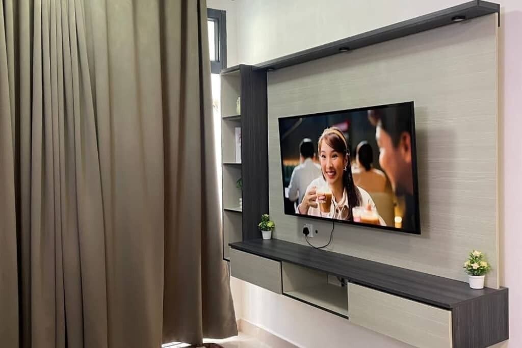 Un salon moderne avec un téléviseur à écran plat fixé au mur, un meuble de rangement en bois foncé en dessous, et une petite plante en pot posée sur le meuble.