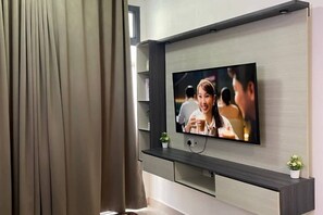 Un soggiorno moderno con una TV a schermo piatto montata a parete, un mobile TV in legno scuro sottostante e una piccola pianta in vaso sopra il mobile.