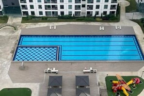Una piscina rettangolare con un motivo a scacchi su un lato, circondata da poltrone a sdraio e ombrelloni.