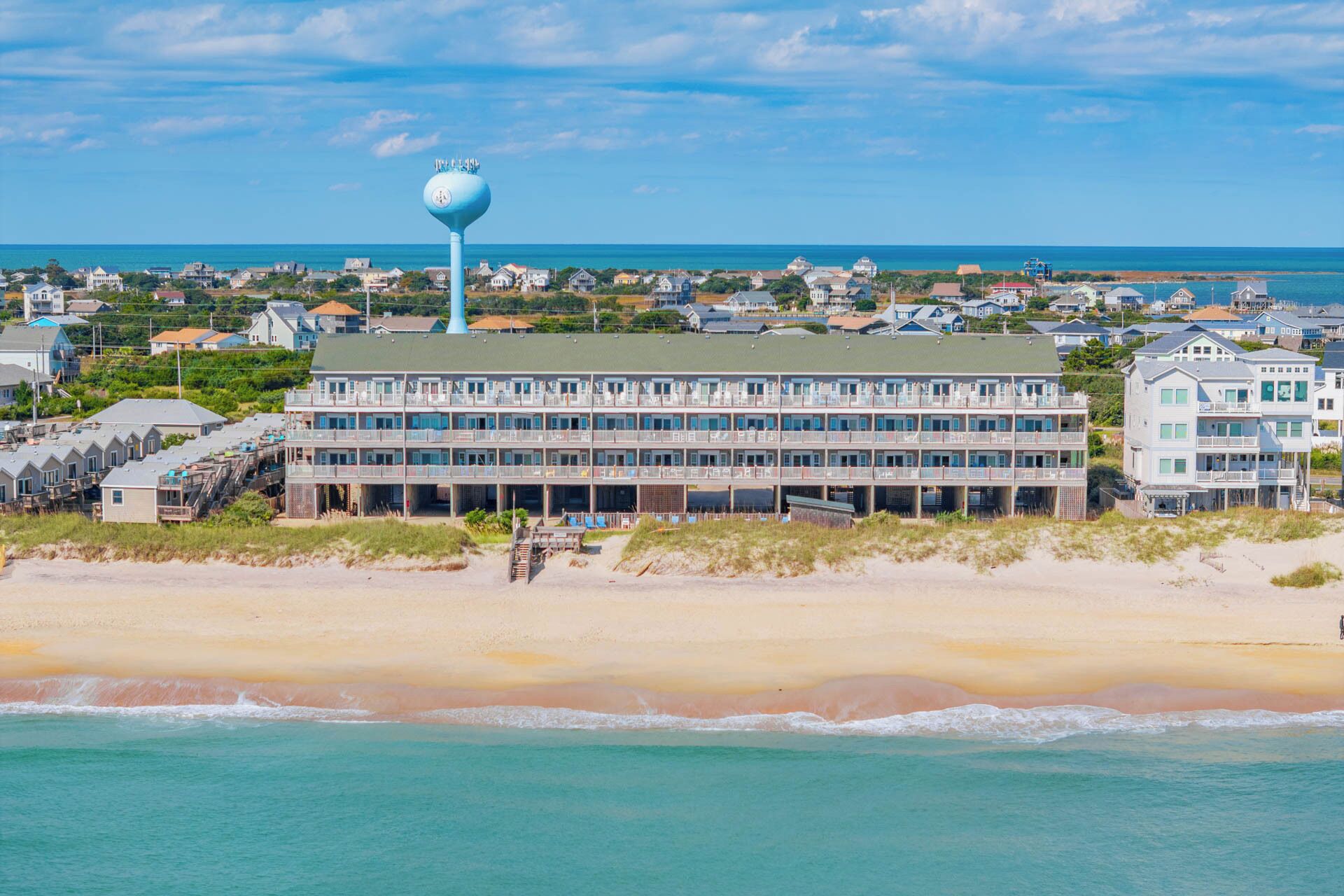 A beachfront hotel with multiple floors, a prominent blue tower, and a view of the ocean.