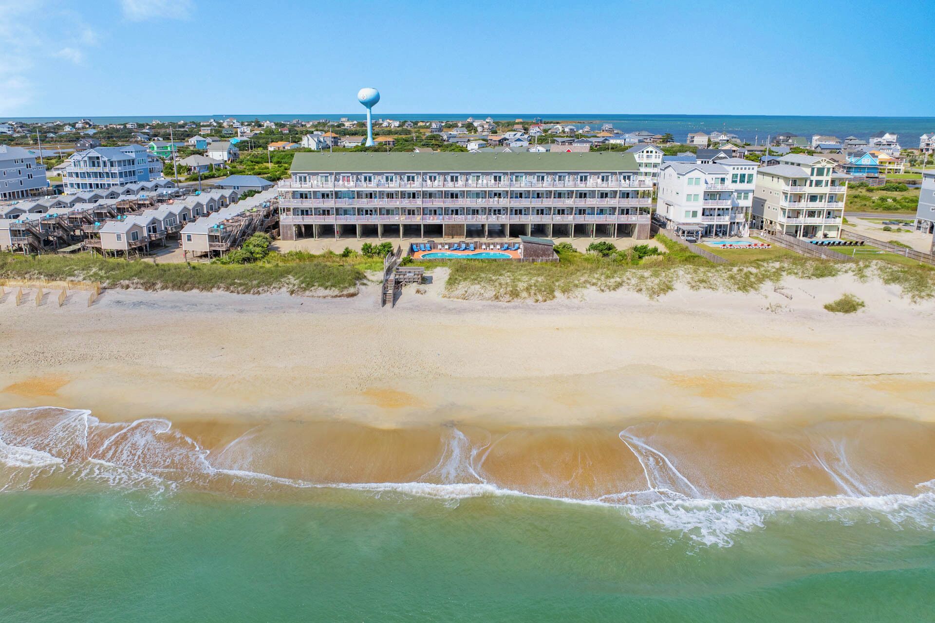 A beachfront hotel with multiple buildings, a swimming pool, and a water tower.
