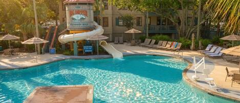 A swimming pool with a water slide, lounge chairs, and umbrellas.