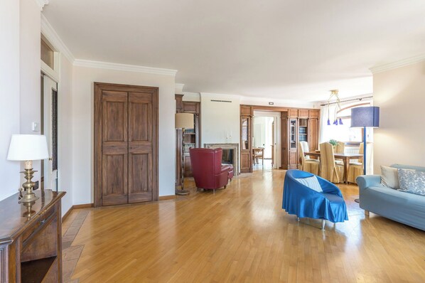 Un salon spacieux doté d’un parquet, d’un fauteuil rouge, d’un canapé bleu et d’un coin repas avec une table et des chaises.